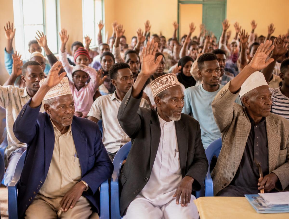 Kenyan elders and youth raising hands during a community town hall meeting